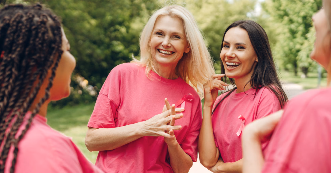 Group of four women stood laughing all wearing pink tops